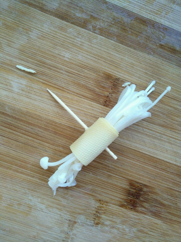 将小朵金针菇对折后,豆腐皮卷紧,再用一根牙签
